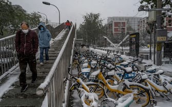 BEIJING, CHINA - NOVEMBER 07: People walk by bicycles covered in snow following a snowfall on November 7, 2021 in Beijing, China.  Beijing, which averages less than seven days of snow annually, is set to host the Beijing 2022 Winter Olympics next February. (Photo by Kevin Frayer/Getty Images)