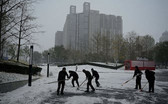 Workers shovel snow in front of a mall in Beijing on November 7, 2021. (Photo by Noel Celis / AFP) (Photo by NOEL CELIS/AFP via Getty Images)