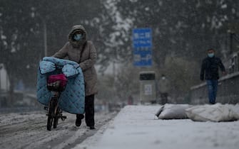 People walk on a street as it snows in Beijing on November 7, 2021. (Photo by Noel Celis / AFP) (Photo by NOEL CELIS/AFP via Getty Images)