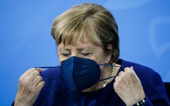 epa09589847 Acting German Chancellor Angela Merkel takes off her face mask during a press conference after a meeting between German State Premiers and acting Chancellor on the occasion of the current coronavirus situation, at the Chancellery in Berlin, Germany, 18 November 2021. Germany is dealing with a high number of new coronavirus COVID-19 infections.  EPA/CLEMENS BILAN / POOL