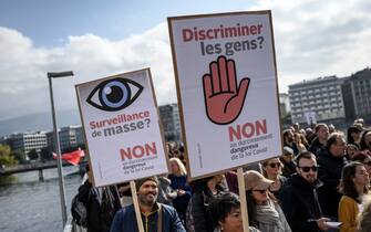 Protesters hold placards reading in French 'Mass monitoring? No to the dangerous tightening of the Covid law' and 'Discriminate against people? No to the dangerous tightening of the Covid law' in Geneva on October 9, 2021, during a rally against coronavirus measures, Covid-19 health pass and vaccination. - On 28 November 2021, Swiss voters will be asked whether they accept laws passed by the government on 19 March 2021 that paved the way for the introduction of Switzerlands Covid certificate, a system that provides proof of vaccination, recovery or a negative test. (Photo by Fabrice COFFRINI / AFP) (Photo by FABRICE COFFRINI/AFP via Getty Images)