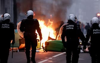 Belgian riot police walk past a burning bins as clashes erupt during a demonstration against Belgian government's measures to curb the spread of the Covid-19 and mandatory vaccination in Brussels on December 5, 2021. - Belgian schools will require children aged six and above to wear masks because of "an autumn wave that has been much tougher than expected," the government says. Indoor venues such as cinemas will be limited to 200 people from December 6, 2021, with people required to be seated and wearing masks. (Photo by Kenzo TRIBOUILLARD / AFP) (Photo by KENZO TRIBOUILLARD/AFP via Getty Images)
