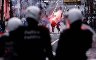 Protesters light flares in front of riot police as clashes erupt during a demonstration against Belgian government's measures to curb the spread of the Covid-19 and mandatory vaccination in Brussels on December 5, 2021. - Belgian schools will require children aged six and above to wear masks because of "an autumn wave that has been much tougher than expected," the government says. Indoor venues such as cinemas will be limited to 200 people from December 6, 2021, with people required to be seated and wearing masks. (Photo by Kenzo TRIBOUILLARD / AFP) (Photo by KENZO TRIBOUILLARD/AFP via Getty Images)