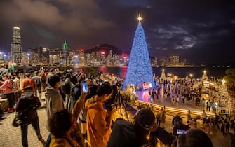 Visitors take photographs of the city's skyline with an illuminated Christmas tree at West Kowloon Cultural District at night in Hong Kong, China, on Tuesday, Dec. 7, 2021. Hong Kong will prioritize quarantine-free travel for business people when its China border reopens, Chief Executive Carrie Lam said, warning that the city’s vaccination rate could curb a broader roll-out. Photographer: Paul Yeung/Bloomberg