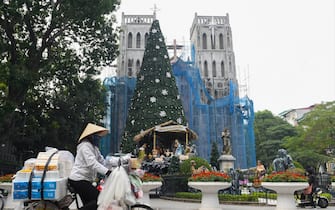 A street vendor rides her bicycle past a Christmas tree displayed in front of St Joseph's cathedral in Hanoi on December 8, 2021. (Photo by Nhac NGUYEN / AFP) (Photo by NHAC NGUYEN/AFP via Getty Images)