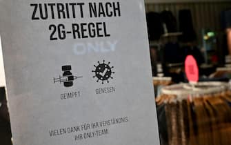 22 December 2021, Bavaria, Munich: A sign reading "Access by 2G Rule - Vaccinated - Recovered" hangs at the entrance to a downtown retail store. Photo: Peter Kneffel/dpa (Photo by Peter Kneffel/picture alliance via Getty Images)