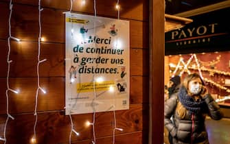 A woman, wearing a face mask as a preventive measure against the Covid-19 coronavirus, walks past a placard reading in French : "Please continue to keep your distance" in a Christmas market in Lausanne on December 2, 2021. - Switzerland announced it was dropping 10-day quarantine rules for people flying in from countries where the Omicron Covid-19 variant has been detected. The wealthy Alpine nation -- one of Europe's top skiing holiday destinations -- said the rule no longer made sense now that the variant is also circulating in Switzerland. (Photo by Fabrice COFFRINI / AFP) (Photo by FABRICE COFFRINI/AFP via Getty Images)