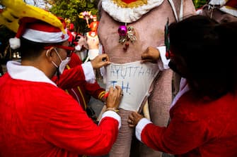 PHRA NAKHON SI AYUTTHAYA, THAILAND - DECEMBER 24: Elephant trainers dress their elephants in Santa Claus costumes before delivering gifts to children at the Jirasat Wittaya elementary school on December 24, 2021 in Phra Nakhon si Ayutthaya, Thailand.  Each year, elephants from the Royal Elephant Palace in Ayutthaya are dressed up in Santa Claus costumes and visit children at the Jirasat Wittaya elementary school to perform and hand out presents.  This year elephants distributed balloons and hand sanitizer to students dressed for the holidays.  (Photo by Lauren DeCicca / Getty Images)