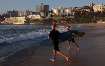 SYDNEY, AUSTRALIA - DECEMBER 25: Surfers in Santa hats make their way to the water at Bondi Beach at sunrise on December 25, 2021 in Sydney, Australia. December is one of the hottest months of the year across Australia, with Christmas Day traditionally involving a trip to the beach and celebrations outdoors. (Photo by Brook Mitchell/Getty Images)