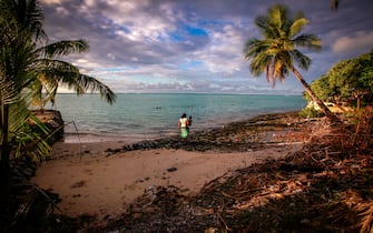 A woman carries her young child as she walks along a small beach covered with sticks and rubbish near the village of Eita on South Tarawa in the central Pacific island nation of Kiribati on May 25, 2013.                                   
