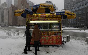 epa09717087 People stop for food at a street vendor at Columbus Circle in New York, New York, USA, 29 January 2022. The large storm is hitting a substantial portion of the East Coast of the United States, disrupting travel and some areas are forecast to receive up to 2 feet (61 centimeters) of snow.  EPA/Peter Foley