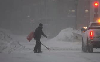 epa09716649 A man navigates the streets while carrying a shovel, in Boston, Massachusetts, USA, 29 January 2022. A winter storm is expected to bring up to 40in (102cm) of snow to the east coast areas of Massachusetts, along with extreme high tides and flooding.  EPA/CJ GUNTHER