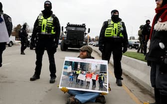 Protestor Paul Acorn sits on the ground in front of police officers as they block the entrance to the Ambassador Bridge in Windsor, Ontario, Canada, on February 12, 2022. - Police in Canada were positioning Saturday to clear the bridge on the US border, snarled for days by truckers protesting against vaccination rules, an AFP journalist observed. "We urge all demonstrators to act lawfully & peacefully," police in Windsor, Ontario, home to the Ambassador Bridge, tweeted in announcing the deployment. (Photo by JEFF KOWALSKY / AFP) (Photo by JEFF KOWALSKY/AFP via Getty Images)