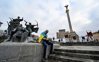 a man wrapped with an Ukrainian national flag watches news on his mobile phone as he sits at Maidan Independence Square in Kyiv on February 24, 2022 as Russia's ground forces invaded Ukraine from several directions today, encircling the country within hours of Russian President announcing his decision to launch an assault. - Heavy Russian tanks and other equipment crossed the frontier in a string of northern regions as well as from the Kremlin-annexed peninsula of Crimea in the south. They were also advancing into the Western-backed government's territory along the eastern front, where a separatist insurgency has claimed more than 14,000 lives since 2014. (Photo by Sergei SUPINSKY / AFP) (Photo by SERGEI SUPINSKY/AFP via Getty Images)