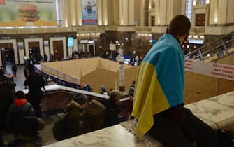 KYIV, UKRAINE - FEBRUARY 24: A man wearing the Ukrainian national flag is waiting for a train at the train station as all trains are delayed on February 24, 2022 in Kyiv, Ukraine. Overnight, Russia began a large-scale attack on Ukraine, with explosions reported in multiple cities and far outside the restive eastern regions held by Russian-backed rebels. (Photo by Pierre Crom/Getty Images)