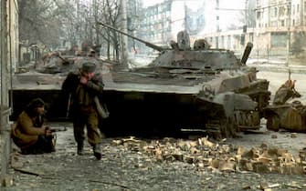 GROZNY, RUSSIA - JANUARY 10:  A Chechen fighter runs for cover as another hides behind a destroyed Russian tank during fighting in Grozny, 08 January. Russian forces resumed shelling the center of Grozny 10 January in violation of a 48-hour unilateral ceasefire offered by the Russian government. (COLOR KEY: Green trousers.)  (Photo credit should read OLEG NIKISHIN/AFP via Getty Images)