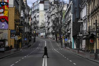 A civilian crosses an empty street in downtown Kyiv, on February 27, 2022. - Kyiv authorities on February 26, 2022 toughened curfew orders in the city, saying violators would be considered "enemy" saboteurs as Russian forces press to capture Ukraine's capital. (Photo by Aris Messinis / AFP)