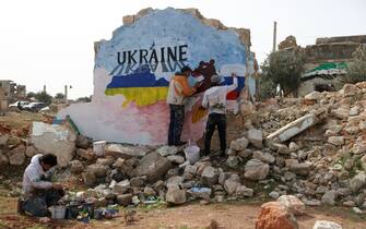 Syrian artists Aziz Asmar and Anis Hamdoun paint a mural amid the destruction, depicting the colours of the Russian and Ukrainian flags, to protest against Russia's military operation in Ukraine, in the rebel-held town of Binnish in Syria's northwestern Idlib province on February 24, 2022. (Photo by OMAR HAJ KADOUR / AFP) (Photo by OMAR HAJ KADOUR/AFP via Getty Images)
