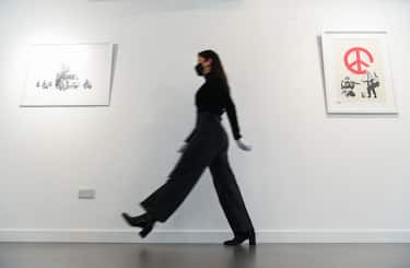 Gallery assistant Sophia Shim walks past limited edition prints of Donuts (Chocolate) (2009, left) and CND Soldiers (2005, right), part of the 'Catch Me If You Can' exhibition, at the HOFA Gallery in Mayfair, London. (Photo by Kirsty O'Connor/PA Images via Getty Images)