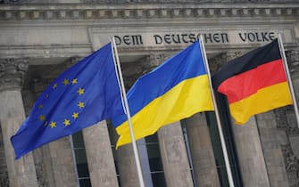 epa09830575 The national flag of the Ukraine (C) waves in front of the Reichstag building on the occasion of the video address of the Ukrainian President to the German parliament in Berlin, Germany, 17 March 2022. Ukrainian President Volodymyr Zelensky addressed the German parliamentarians after Russian troops had entered Ukrainian territory on 24 February in what the Russian president declared a 'special military operation', resulting in fighting and destruction in the country, a huge flow of refugees, and multiple sanctions against Russia.  EPA/CLEMENS BILAN