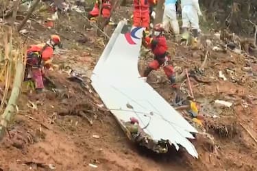 This screengrab taken on March 24, 2022 from video by state broadcaster China Central Television (CCTV) via AFPTV shows rescue teams with a piece of the fuselage as they continue their search at the site of where a China Eastern passenger jet crashed onto a mountainside near Wuzhou City in China's southern Guangxi region. - The cause of the disaster which killed 132 people has mystified aviation authorities who have scoured rugged terrain for clues, finding no survivors from what is almost certain to be China's deadliest plane crash in nearly 30 years. - China OUT (Photo by various sources / AFP) / China OUT (Photo by STR/AFPTV/AFP via Getty Images)
