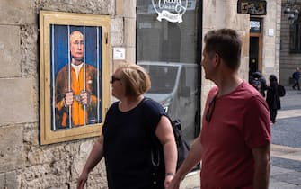 People look on while walking past a portrait of Vladimir Putin behind the bars.  Vladimir Putin behind bars is represented in the new public graphic collage in Plaza de Sant Jaume by Barcelona-based Italian artist TvBoy.  (Photo by Paco Freire / SOPA Images / Sipa USA)