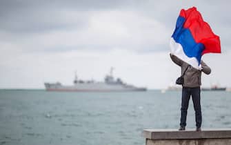 A man poses with a Russian flag in front of a ship of the Russian Black Sea Fleet in Sevastopol, Crimea, Ukraine, 16 March 2014. Polling stations opened in Crimea for a referendum about whether the Ukrainian Black Sea region should join Russia. The vote has been widely condemned by Western governments, who call it illegal and have announced sanctions against Russia if it goes ahead. Thousands of unmarked forces, believed to be Russian, have appeared in Crimea after local Moscow-backed authorities asked Russia for protection against 'extremists' in the new Ukrainian leadership. Photo: Hannibal/dpa