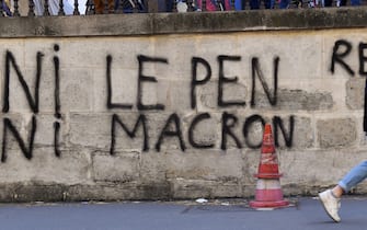 A pedestrian walks ahead a graffiti write "Neither Le Pen nor Macron" during a demonstration organized by activits of the climate change action group Extinction Rebellion in Paris, on April 16 2022. - A few hundred activists from the environmental group Extinction Rebellion set up shop on April 16, 2022 morning on part of the Grands Boulevards, in the center of Paris, in order to make it "a great agora" on the climate during the Easter weekend.  (Photo by JULIEN DE ROSA / AFP) (Photo by JULIEN DE ROSA / AFP via Getty Images)