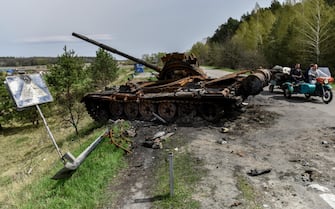 epa09908824 People ride a motorcycle on a road near destroyed Russian tank in recaptured by the Ukrainian army Rusaniv village of Kyiv area, Ukraine, 25 April 2022. Russian troops entered Ukraine on 24 February resulting in fighting and destruction in the country, and triggering a series of severe economic sanctions on Russia by Western countries.  EPA/OLEG PETRASYUK