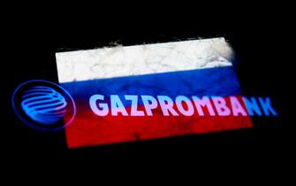 Gazprombank logo displayed on a phone screen and Russian flag displayed on a phone screen are seen in this multiple exposure illustration photo taken in Krakow, Poland on March 31, 2022. (Photo illustration by Jakub Porzycki/NurPhoto via Getty Images)