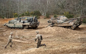 Soldiers run across the training ground as they take part in an exercise to winch an overturned battle tank using a CrARRV (Challenger Armoured Repair and Recovery Vehicle) during the Royal Electrical & Mechanical Engineers Exercise called "Iron Challenge" at the Longmoor training area, near Bordon, Hampshire, on March 14, 2022. (Photo by ADRIAN DENNIS / AFP) (Photo by ADRIAN DENNIS/AFP via Getty Images)