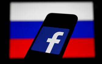 Facebook logo displayed on a phone screen and Russian flag displayed on a screen in the background are seen in this illustration photo taken in Krakow, Poland on March 1, 2022. (Photo Illustration by Jakub Porzycki/NurPhoto via Getty Images)