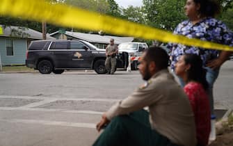 People sit on the curb outside of Robb Elementary School as State troopers guard the area in Uvalde, Texas, on May 24, 2022. - An 18-year-old gunman killed 14 children and a teacher at an elementary school in Texas on Tuesday, according to the state's governor, in the nation's deadliest school shooting in years. (Photo by allison dinner / AFP) (Photo by ALLISON DINNER/AFP via Getty Images)