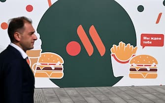 An employee stands in front of the new logo of the Russian version of a former McDonald's restaurant before the opening ceremony, in Moscow on June 12, 2022. (Photo by Kirill KUDRYAVTSEV / AFP)