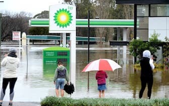 People stand next to a flooded petrol station due to torrential rain in the Camden suburb of Sydney on July 3, 2022. - Thousands of Australians were ordered to evacuate their homes in Sydney on July 3 as torrential rain battered the country's largest city and floodwaters inundated its outskirts. (Photo by Muhammad FAROOQ / AFP) (Photo by MUHAMMAD FAROOQ/AFP via Getty Images)