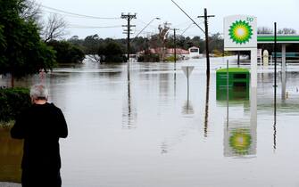 A man stand next to a flooded petrol station due to torrential rain in the Camden suburb of Sydney on July 3, 2022. - Thousands of Australians were ordered to evacuate their homes in Sydney on July 3 as torrential rain battered the country's largest city and floodwaters inundated its outskirts. (Photo by Muhammad FAROOQ / AFP) (Photo by MUHAMMAD FAROOQ/AFP via Getty Images)