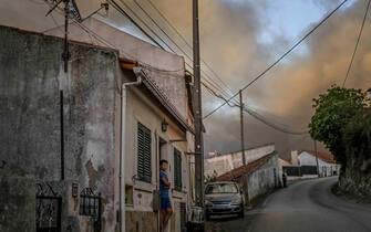 TOPSHOT - A boy stands at his house's front door watching the progression of a wildfire in Mafra on July 31, 2022. (Photo by PATRICIA DE MELO MOREIRA / AFP) (Photo by PATRICIA DE MELO MOREIRA/AFP via Getty Images)