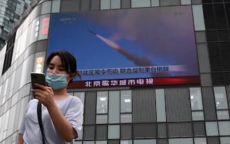 1242298521 A woman uses her mobile phone as she walks in front of a large screen showing a news broadcast about China's military exercises encircling Taiwan, in Beijing on August 4, 2022. - China's largest-ever military exercises encircling Taiwan kicked off August 4, in a show of force straddling vital international shipping lanes after a visit to the island by US House Speaker Nancy Pelosi. (Photo by Noel Celis / AFP) (Photo by NOEL CELIS/AFP via Getty Images)