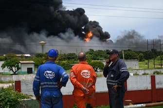 Workers of Cuban Petroleum (CUPET) look at the black smoke near the fire at oil tanks in Matanzas, Cuba, on August 6, 2022. - The fire caused by lightning on Friday in a fuel depot in Matanzas, in western Cuba, spread to a second tank at dawn this Saturday and caused 49 injuries, official sources reported. (Photo by YAMIL LAGE / AFP) (Photo by YAMIL LAGE/AFP via Getty Images)