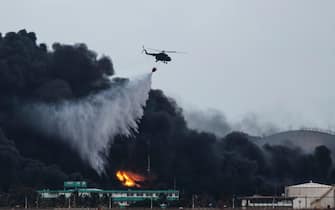 A firefighter helicopter drops water on a massive fire at a fuel depot in Matanzas, Cuba, on August 8, 2022. - Helicopters scrambled to contain a days-old blaze that felled a third tank at a fuel depot on Monday as the search continued for 16 missing firefighters. (Photo by YAMIL LAGE / AFP) (Photo by YAMIL LAGE/AFP via Getty Images)