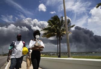 MATANZAS, CUBA - AUGUST 08: Several people walk with masks while black clouds are seen over the bay of Matanzas during the third day of the fire of several fuel tanks, in Matanzas, today, Monday, August 8, 2022. (Photo by Yander Zamora / Anadolu Agency via Getty Images)
