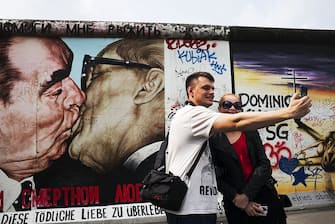 BERLIN, GERMANY - JULY 2014: Tourists take a selfie by Russian painter Dimitri Vladimiorvich Vrubel's most famous work known as 'My God, help me to survive this deadly love' on a section of the former Berlin Wall at the East Side Gallery in Berlin. At Midnight on November 9th, 1989, East Germany's Communist rulers ordered the gates along the Berlin Wall to be opened and thousands of jubilant people surged through to be met by cheering West Berliners on the other side of the 45km barrier dividing the city. The dramatic events of that night marked the end of the Cold War. The wall was erected in 1961 to prevent people leaving East Germany for the West. In nearly 3 decades at least 136 people were killed trying to cross from East to West Berlin. (Photo by Tom Stoddart/Getty Images) .