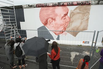 BERLIN - JUNE 22:  Tourists look at the work in progress by Russian artist Dmitry Vrubel showing former Soviet leader Leonid Brezhnev (L) kissing former communist East German leader Erich Honecker at a surviving portion of the Berlin Wall on June 22, 2009 in Berlin, Germany. The painting is on a portion of the Wall known as the East Side Gallery, and city authorities have invited artists to redo their works as part of a restoration effort. The Berlin Wall was built by the East German government and divided East and West Berlin from 1961 until 1989. Germany will mark 20 years since the fall of the Berlin Wall this year with an international commemoraiton in November.  (Photo by Sean Gallup/Getty Images)