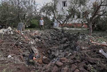 epa10132202 A local man looks on as police inspect a crater at the site of a rocket impact near a private building not far from Kharkiv, Ukraine, 21 August 2022 amid Russia's military invasion. Some rockets were launched from the Russian city of Belgorod. At least two civilians were injured during the attack, emergency service said. Kharkiv and surrounding areas have been the target of heavy shelling since February 2022, when Russian troops entered Ukraine starting a conflict that has provoked destruction and a humanitarian crisis.  EPA/SERGEY KOZLOV