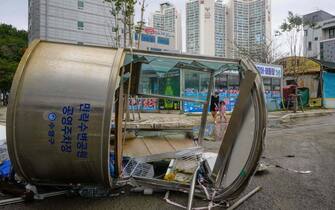 A woman and a child (back C) walk behind a public parking facility booth that was blown over when Typhoon Hinnamnor passed through Busan on September 6, 2022. (Photo by Anthony WALLACE / AFP) (Photo by ANTHONY WALLACE / AFP via Getty Images )