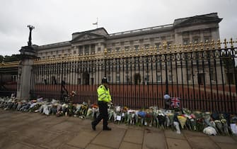 epa10172575 A member of the police force walks past floral tributes that have been left outside the railings of Buckingham Palace, London, Britain, 09 September 2022. Britain's Queen Elizabeth II died at her Scottish estate, Balmoral Castle, on 08 September 2022. The 96-year-old Queen was the longest-reigning monarch in British history.  EPA/NEIL HALL