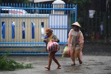 Two residents carrying supplies walk in the rain outside a primary school being used as a shelter during Typhoon Noru in Hoi An in Vietnam's Quang Nam province on September 27, 2022. - Vietnam has tried to evacuate almost 400,000 people ahead of the arrival of typhoon Noru, one of the biggest to make landfall in the country, authorities said on September 27. (Photo by Nhac NGUYEN / AFP) (Photo by NHAC NGUYEN/AFP via Getty Images)