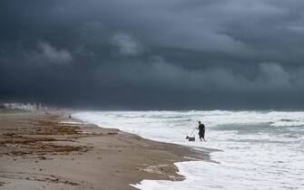 1243574713 A man walks his dog through the rough surf on Cocoa Beach on September 28, 2022, as the eastern coast of central Florida braces for Hurricane Ian. - Heavy winds and rain pummelled Florida on Wednesday as Hurricane Ian intensified to just shy of the strongest Category 5 level, threatening to wreak "catastrophic" destruction on the southern US state. Forecasters warned of a looming once-in-a-generation calamity, with life-threatening storm surges, extensive flooding and devastating winds promising what Florida Governor Ron DeSantis called a "nasty" natural disaster. (Photo by Jim WATSON / AFP) (Photo by JIM WATSON/AFP via Getty Images)