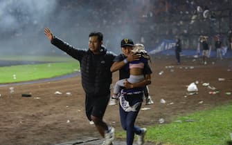 epa10218883 Soccer fans evacuate a girl during a clash between fans at Kanjuruhan Stadium in Malang, East Java, Indonesia 02 October 2022. At least 127 people including police officers were killed mostly in stampedes after a clash between fans of two Indonesian soccer teams, according to the police.  EPA/H. PRABOWO