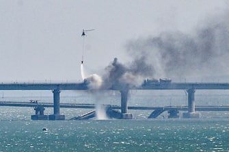 epaselect epa10230640 A firefighter helicopter pours water on fire on a collapsed part of the Kerch Strait bridge in Crimea, 08 October 2022. According to Russian authorities, "an explosion was set off at a cargo vehicle on the motorway part of the Crimean bridge on the side of the Taman peninsula, which set fire to seven fuel tanks of a train that was en route to the Crimean peninsula. Two motorway sections of the bridge partially collapsed."  EPA/STRINGER